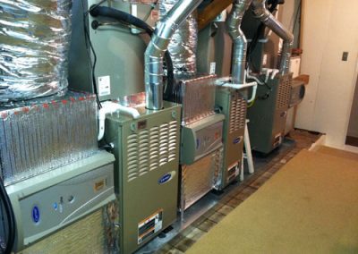 Three HVAC units with ductwork and insulation in a utility room, expertly installed by an HVAC contractor. Carpeted flooring is visible to the right, ensuring warmth and comfort, ideal for homes in Orange County, California.