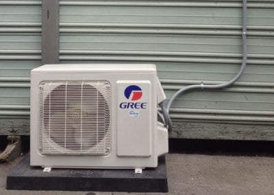 GREE air conditioning unit installed outside on a concrete slab, with connecting pipes attached to a corrugated wall, perfect for California homes in Orange County.