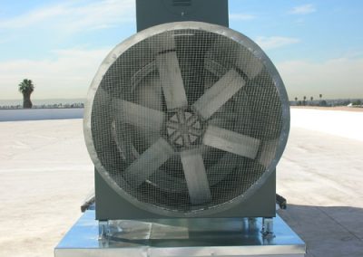 Large industrial exhaust fan secured with metal mesh, placed on a metal platform outdoors, with a clear California sky in the background.