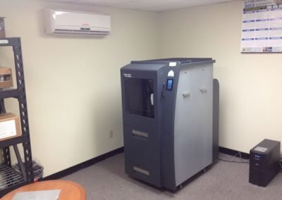 A 3D printer in a small office with a calendar on the wall, air conditioner managed by CA's top residential HVAC contractor, shelving unit, and a computer tower.