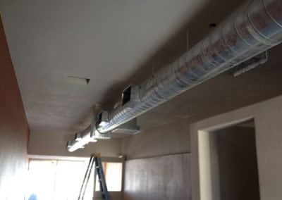 A hallway with installed ventilation ducts on the ceiling, typical of work by an Orange County residential HVAC contractor, and a ladder in the background.