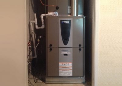 A York-branded furnace, expertly installed by a local HVAC contractor in California, nestles into a small utility area with surrounding pipes and ventilation ducts, ensuring optimal residential HVAC performance.