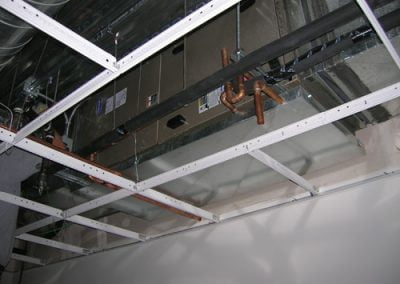 Exposed ceiling with metal framework and HVAC ducts and pipes installed by a top-notch HVAC contractor in Orange County, lacking ceiling tiles or panels.