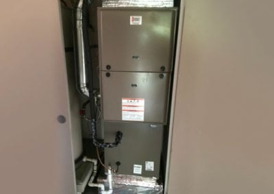 A beige HVAC system, complete with air conditioning, is installed in an indoor utility closet in California, featuring visible pipes and ductwork.