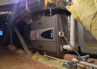 A furnace installed in an attic with insulation on the walls and pipes surrounding it by an HVAC contractor in Orange County, California.