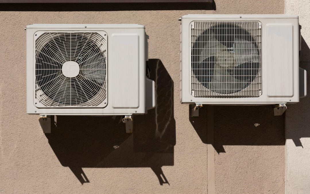 Two wall-mounted air conditioning units cast shadows on a beige wall, reminiscent of cooling solutions perfected by an experienced California HVAC contractor.