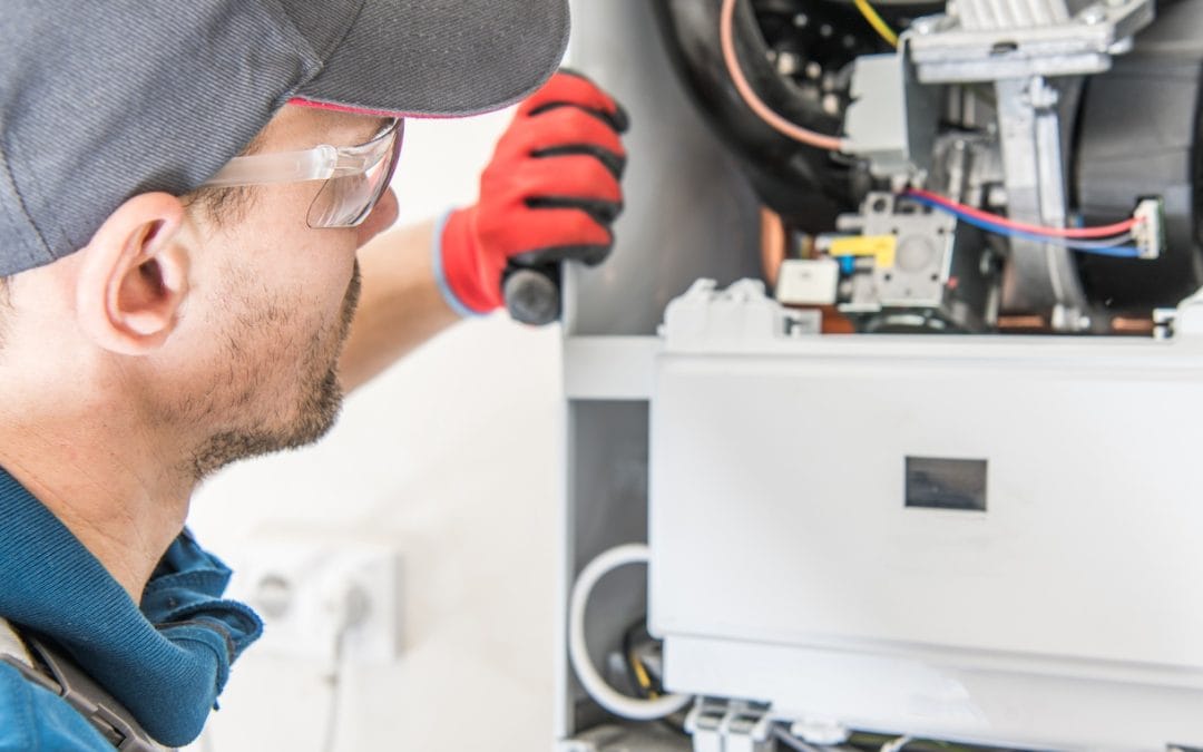 furnace inspections Technician in cap and gloves inspecting HVAC system components inside a unit.