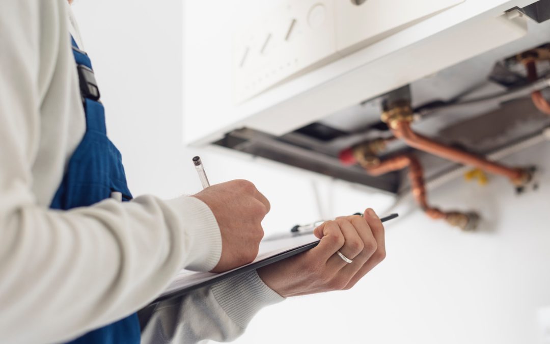 heating services Technician in blue overalls inspects a heating system, taking notes on a clipboard.